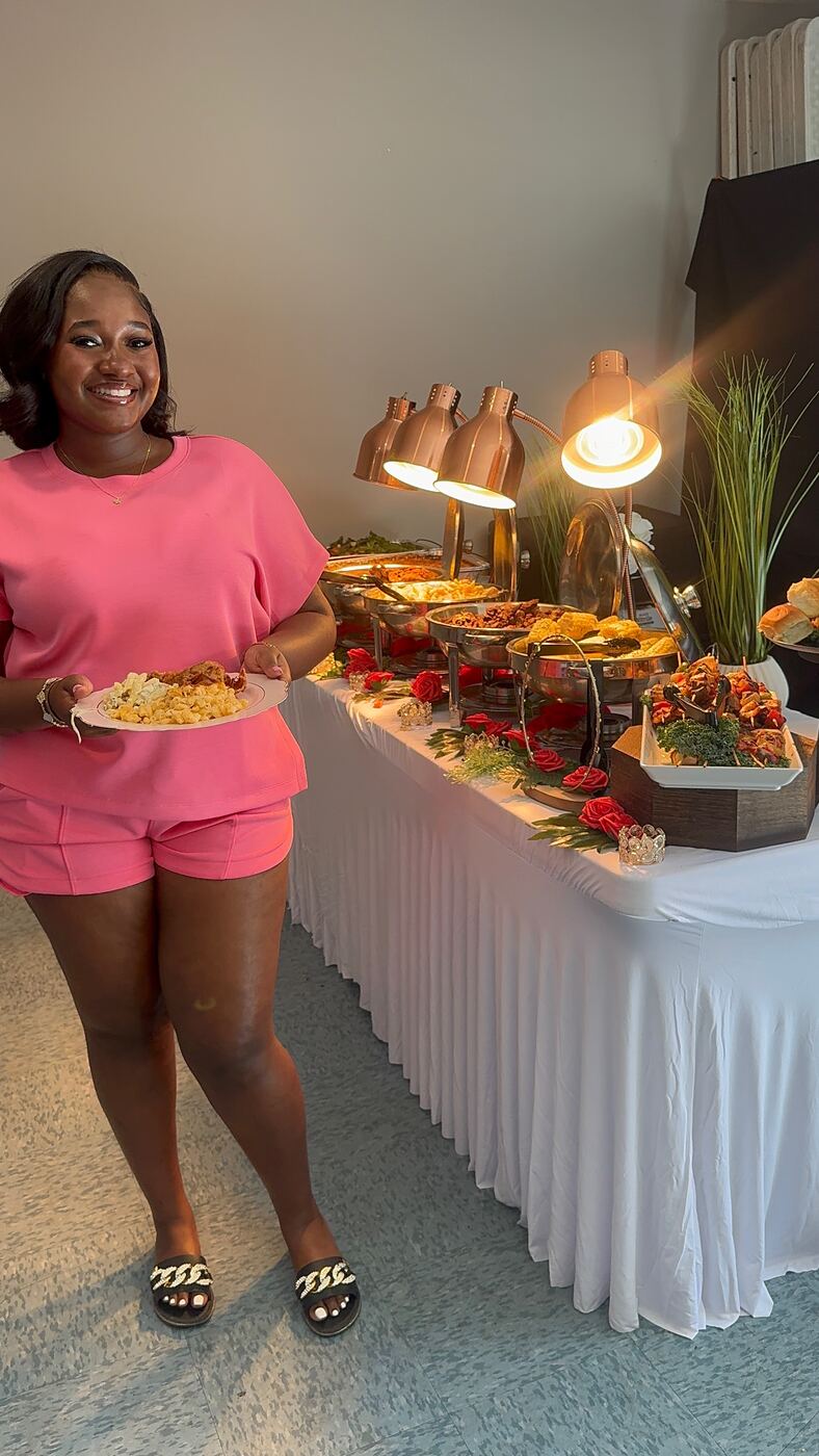 Smiling guest in pink holding her plate at a catered buffet lit by heat lamps