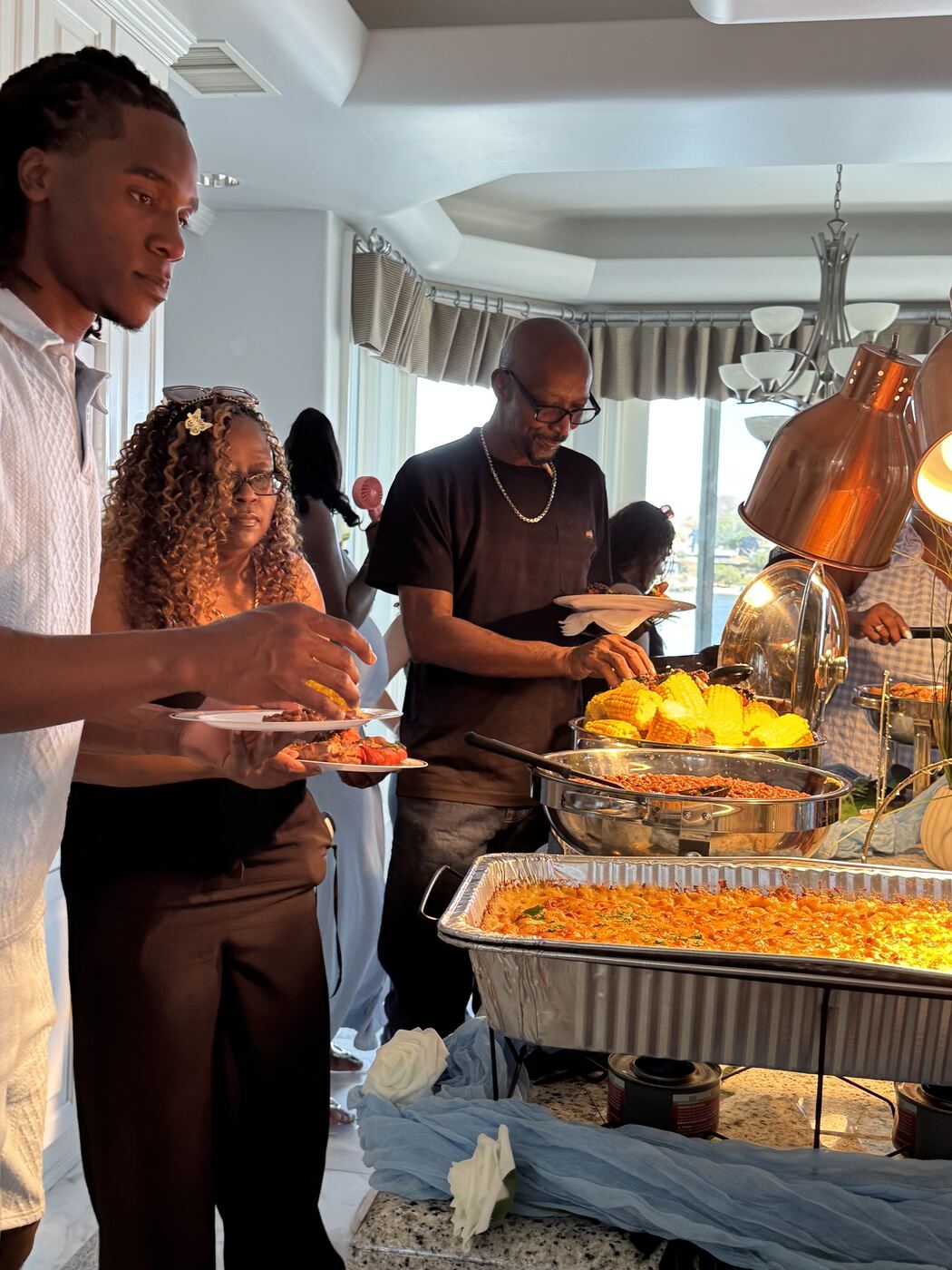 Guests serving corn and pasta along a catered buffet line