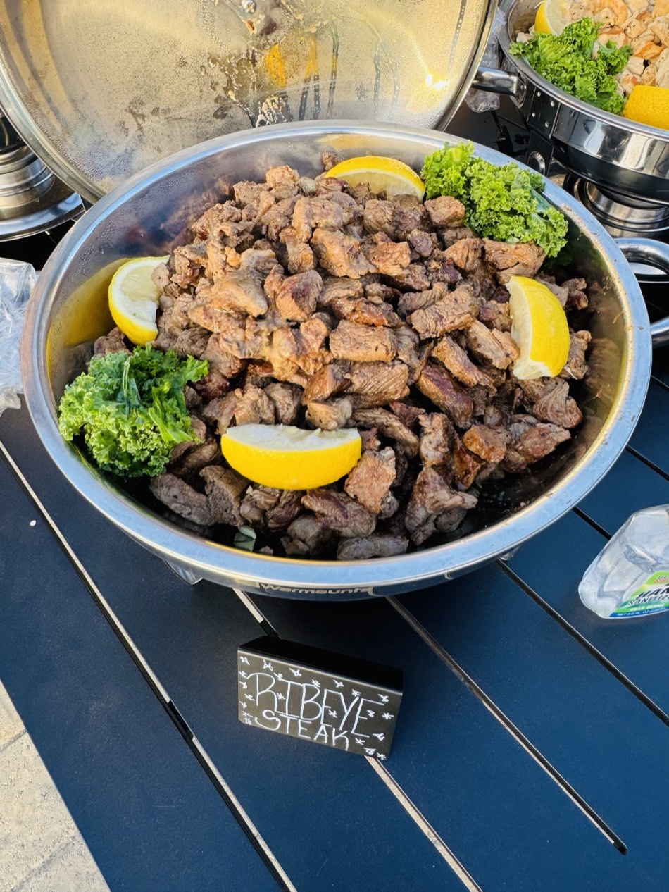 Chafing dish piled with ribeye steak, lemon and greens